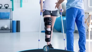 بیماری بعد از عمل جراحی زانو که به کمک فیزیوتراپ در حال راه رفتن است| ژین طب